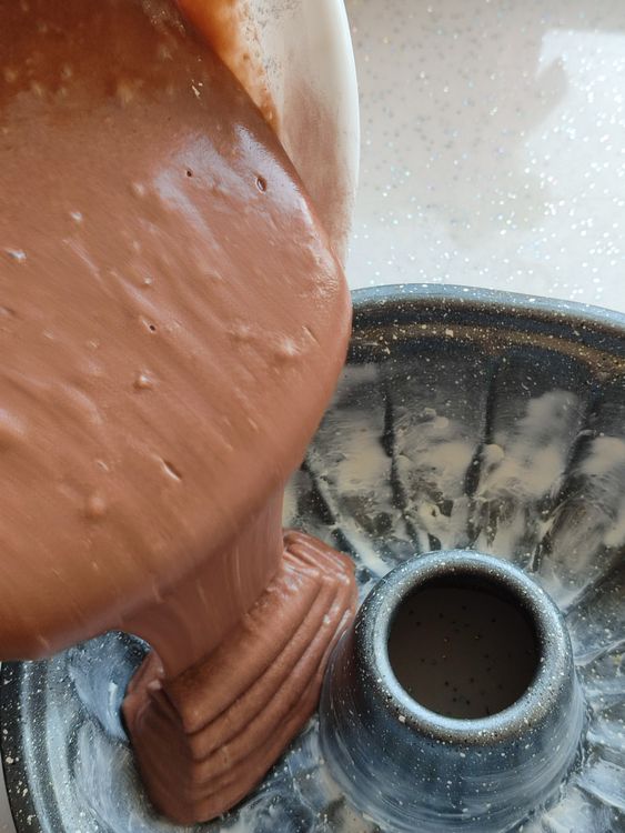 Massa de bolo de chocolate sendo despejada em forma redonda com furo central untada
