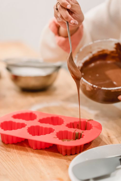 Massa de chocolate sendo despejada em forminhas de silicone vermelhas